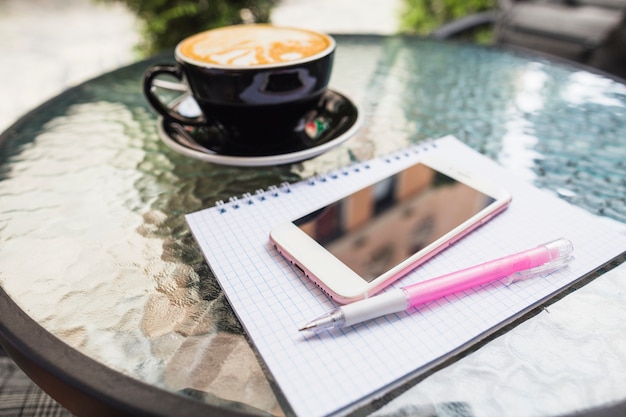 Free Photo mobile on checked notebook and pen with coffee on an outdoors table