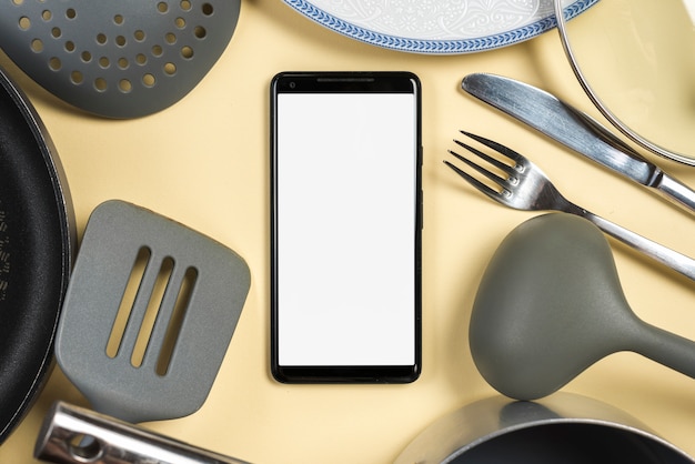 Mobile phone surrounded with utensil on beige background