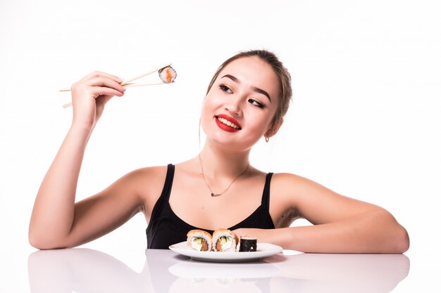 Model asian look with modest hairdo sit on the table eat sushi rolls smiling isolated on white