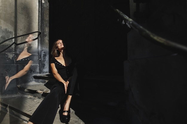 Model dressed in the black outfit sits on the old building stairs