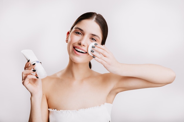 Model with green eyes with on white wall. Brunette moisturizes face with Dove cream.