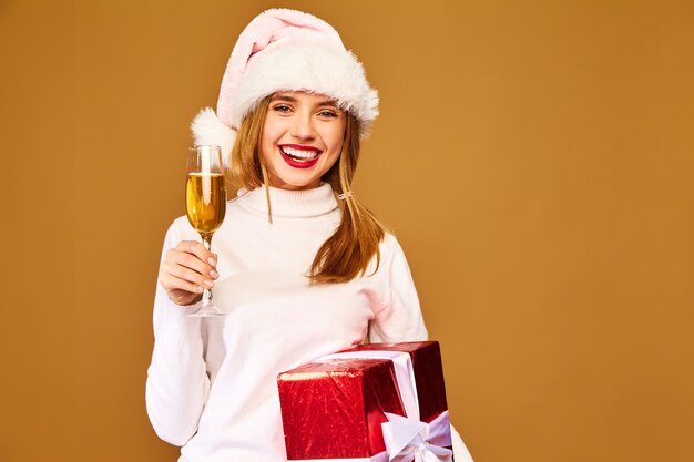 Model with santa hat and big gift box drinking champagne on golden wall