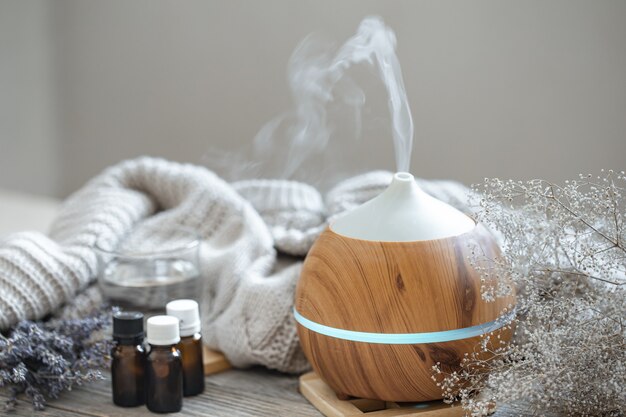 Modern aroma oil diffuser on wood surface with knitted element, water and oils in jars.