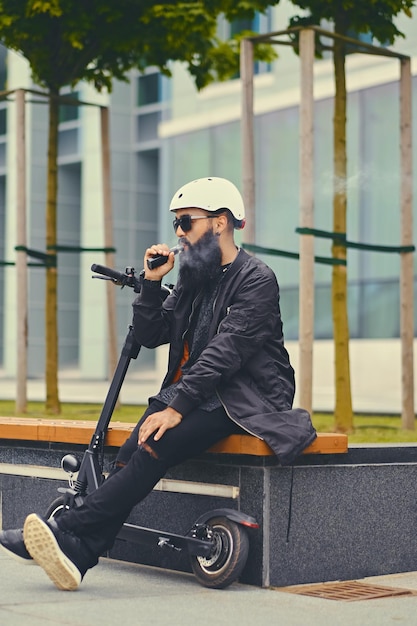 Free photo modern bearded male vaping after electric scooter.