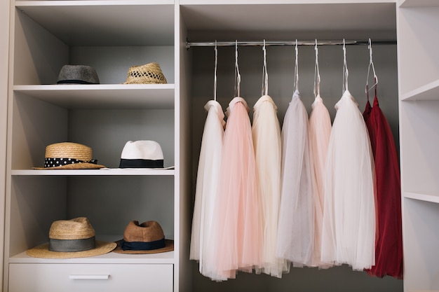 Free photo modern bright dressing room with shelves. fashionable hats, beautiful pink and red dresses hanging in wardrobe.