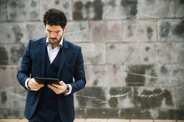 Free photo modern businessman using tablet in front of wall