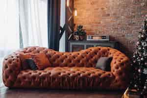 Free photo modern fashionable red leather couch with cushions. cropped christmas tree. brick wall. loft design.