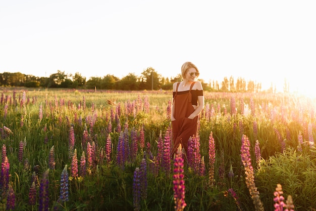 Free photo modern hipster girl walking in wildflower field at sunset.