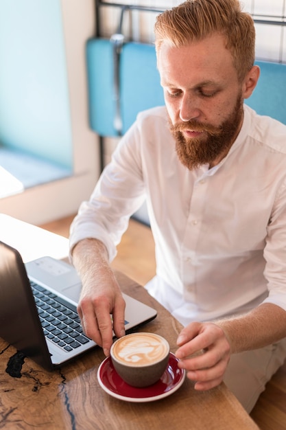 Modern man placing his cup of coffee next to his laptop