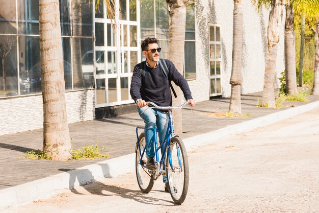 Modern man wearing sunglasses riding bicycle on street