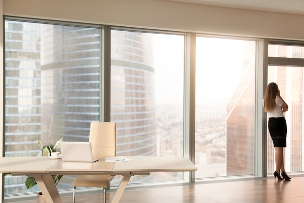 Modern office interior with female silhouette standing at full-length window