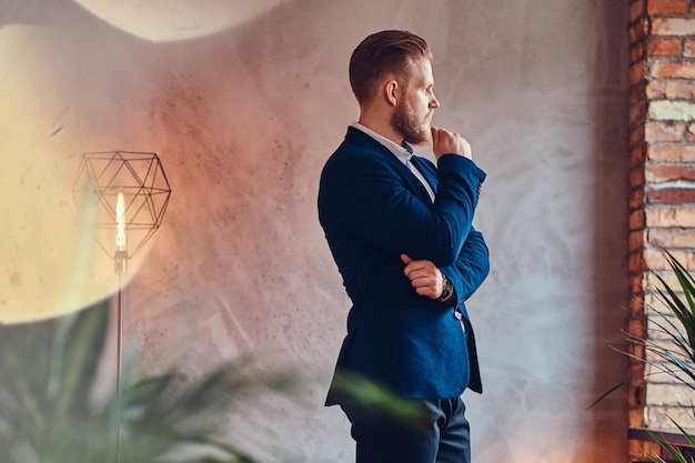 A modern, stylish male dressed in an elegant suit posing in a room with loft interior.