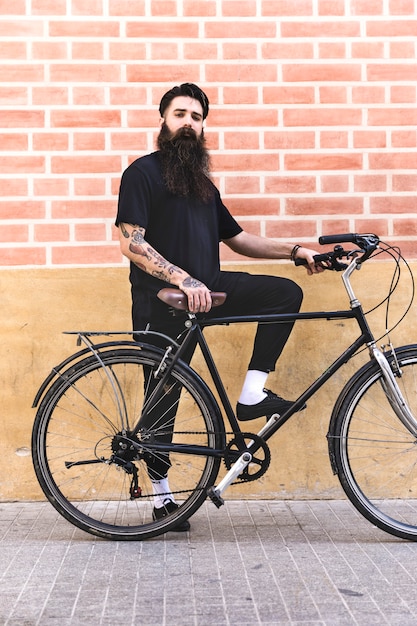 Modern young man standing with his bicycle against brick wall