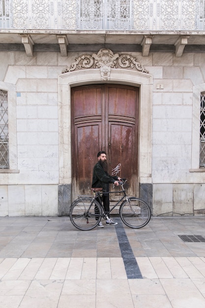 Modern young man with his bicycle standing in front of closed door