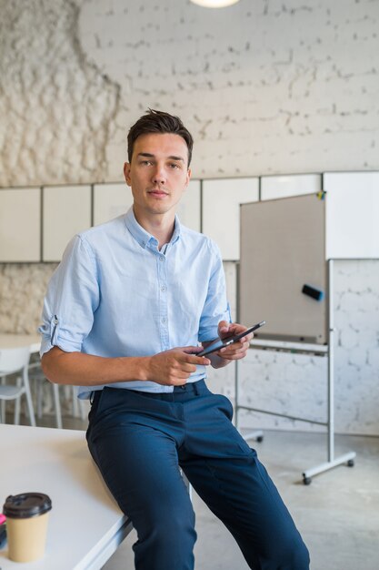 Modern young stylish smiling man in co-working office, startup freelancer holding using tablet,