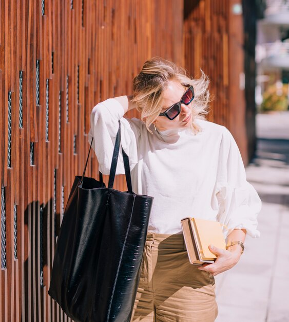 Modern young woman carrying black handbag and holding books looking away