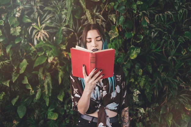 Modern young woman reading book standing in front of growing plants