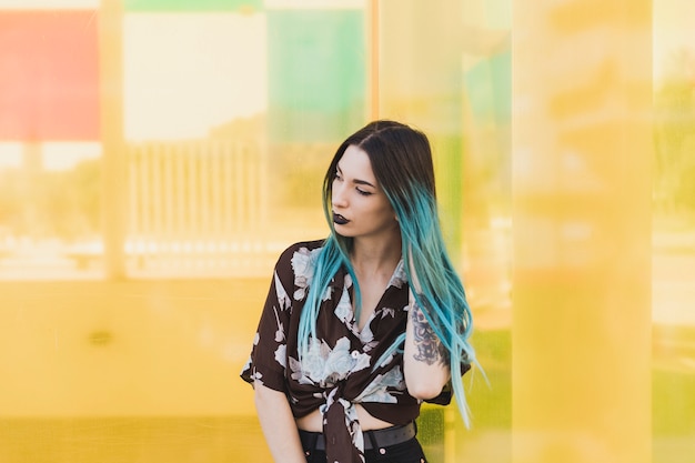 Free photo modern young woman with dyed hair standing in front of yellow background