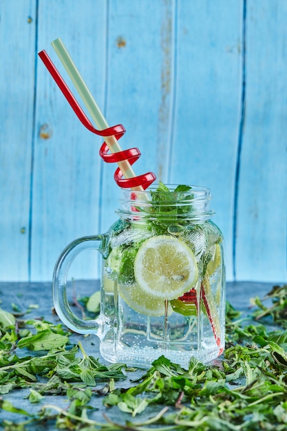 Mojito cocktail with slices of lime and mint on blue table with fresh mint leaves 