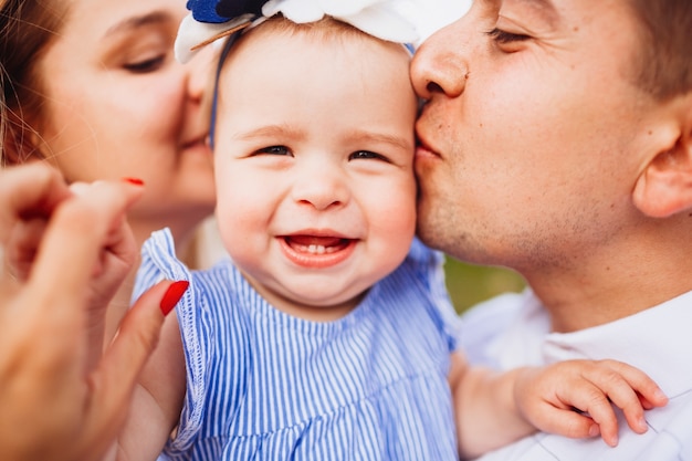 Mom and dad kiss tender little smiling girl in blue dress