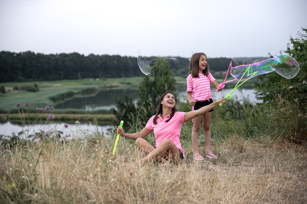 Mom and daughter have fun together, make big soap bubbles, outdoor recreation.