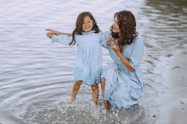 Mom and daughter in identical dresses. Family playing by the river.