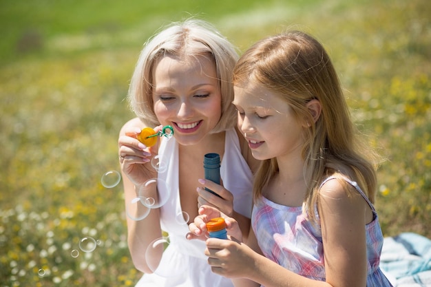 Mom and daughter outdoors. Mother and her child girl playing with bubble blower.