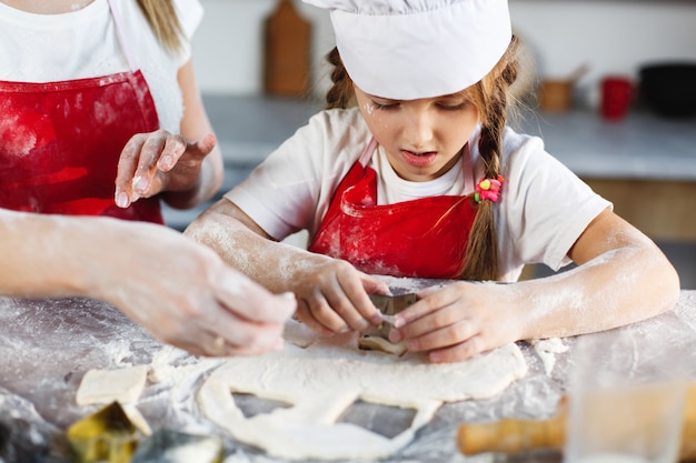 Mom and daughter in the same clothes have fun preparing a dough on a cosy kitchen