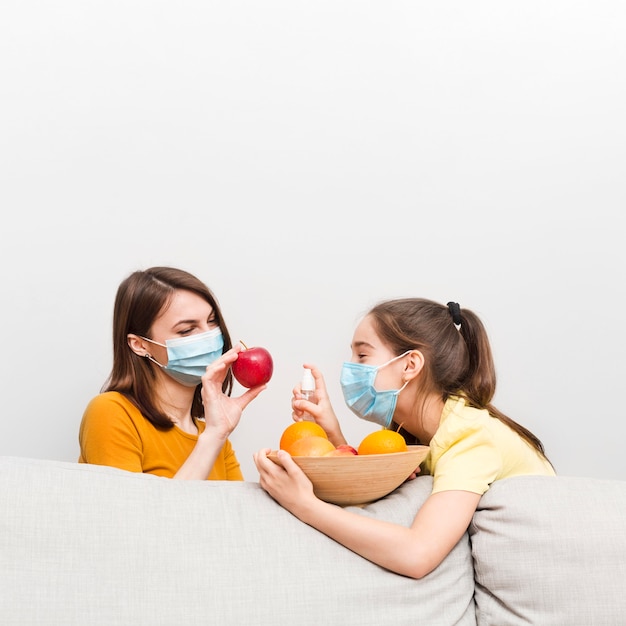 Mom and girl with mask and fruits at home