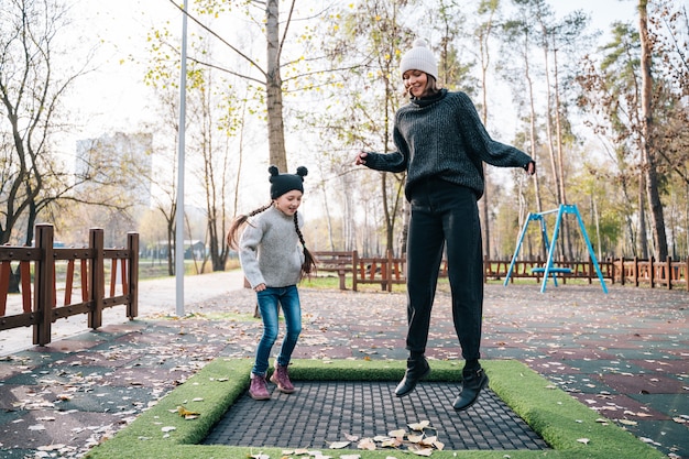 Mom and her daughter jumping together on trampoline in autumn park