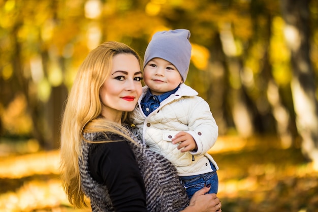 Mom and her son are in the autumn park, the son loves looking at his mother, the woman is holding his hands