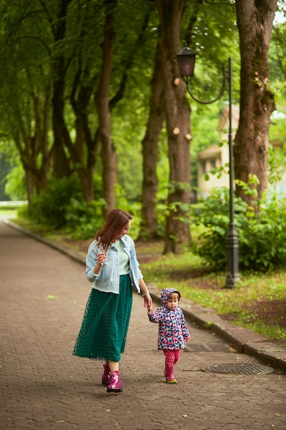 Mom holds daughter's hand walking with her in the park after rain