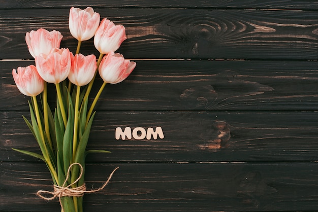 Mom inscription with tulips bouquet on table