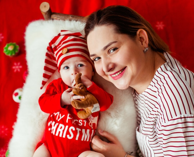 Mom lies before her funny daughter in a red suit with lettering 'My first Christmas' 