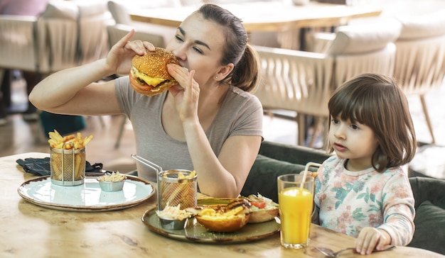 Mom with a cute daughter eating fast food in a cafe