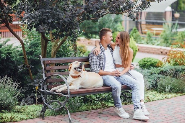 The moment of resting! Beautiful smiling couple with their dog in the park on a sunny day