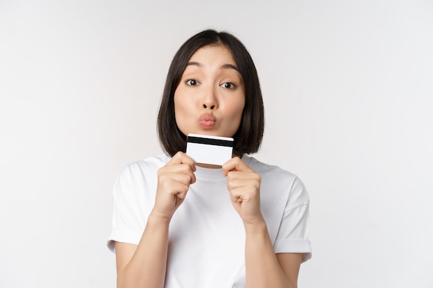 Money and finance concept Cute japanese girl kissing her credit card standing in tshirt over white background