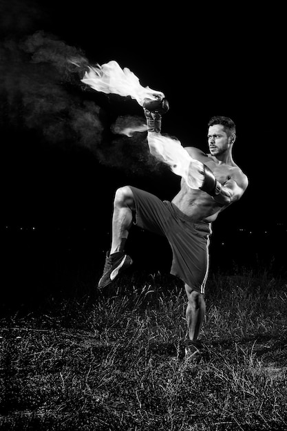 Free Photo monochrome shot of a shirtless muscular strong young male boxer practicing outdoors with his boxing gloves flaming with fire burning burn fiery force confidence martial combat fit muscles sweat agile.