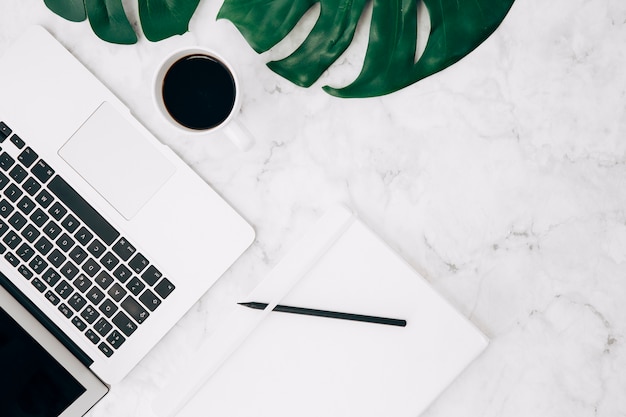 Free photo monstera leaf; coffee; laptop; pencil and diary on marble textured backdrop