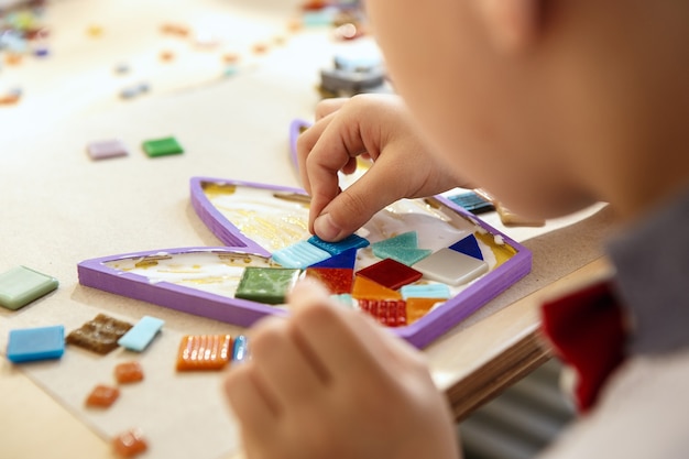 The mosaic puzzle art for kids, children's creative game. The hands are playing mosaic at table. Colorful multi-colored details close up. Creativity, children's development and learning concept