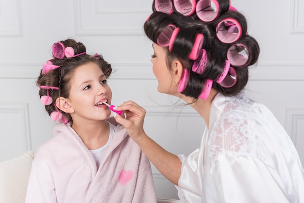 Free photo mother applying pink lip gloss on daughters lips