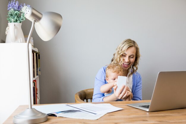 Mother and baby sitting at table and using mobile phone