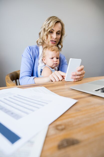 Mother and baby sitting at table and using mobile phone