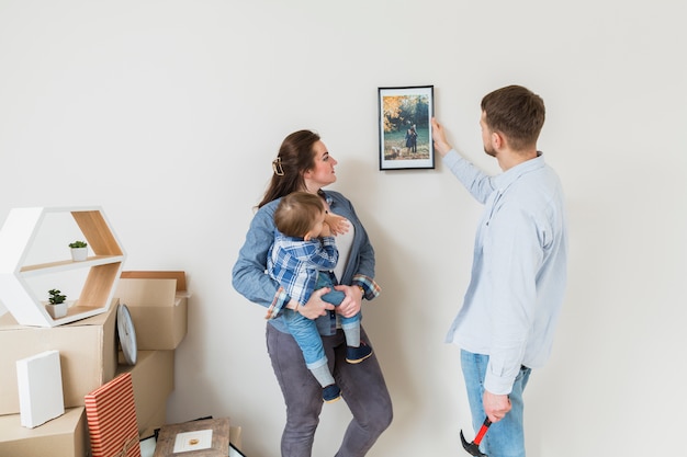 Mother carrying her son looking at frame attached by his husband on wall