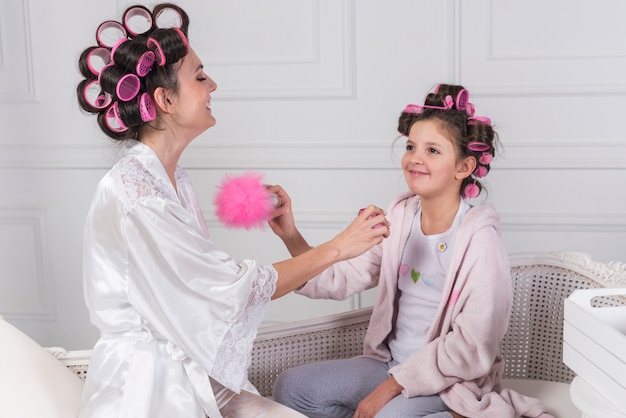 Free photo mother in curlers applying perfume on daughters neck