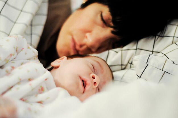 Mother and cute little baby girl sleeping together on bed. 