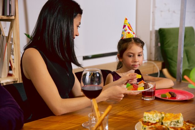 Mother and daughter celebrating a birthday at home. Big family eating cake and drinking wine while greeting and having fun children. Celebration, family, party, home, childhood, parenthood concept.