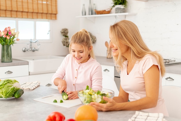 Free photo mother and daughter cutting vegetables together