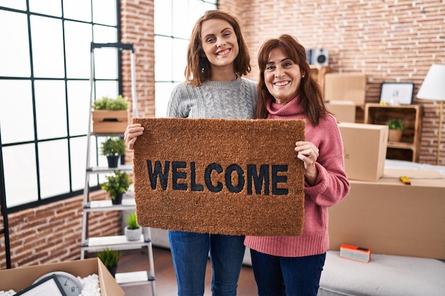 Free photo mother and daughter holding welcome doormat smiling with a happy and cool smile on face. showing teeth.