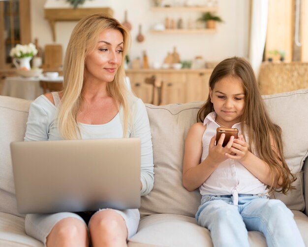 Mother and daughter at home with laptop and smartphone